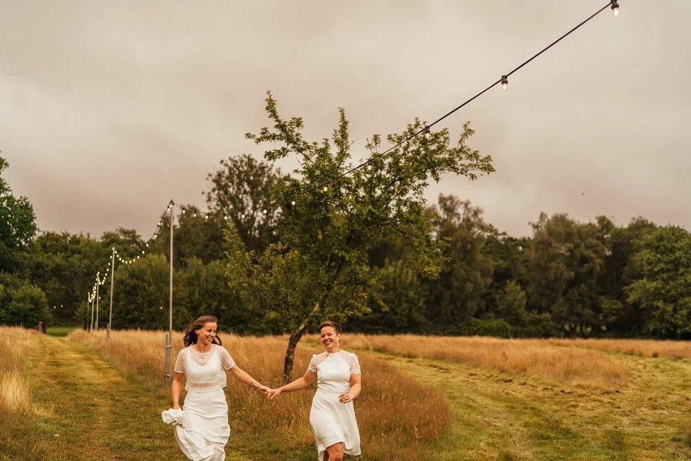 Two brides holding hands, running through the grounds at Glanrennell park house. Happy, smiling couple after an outdoor ceremony.