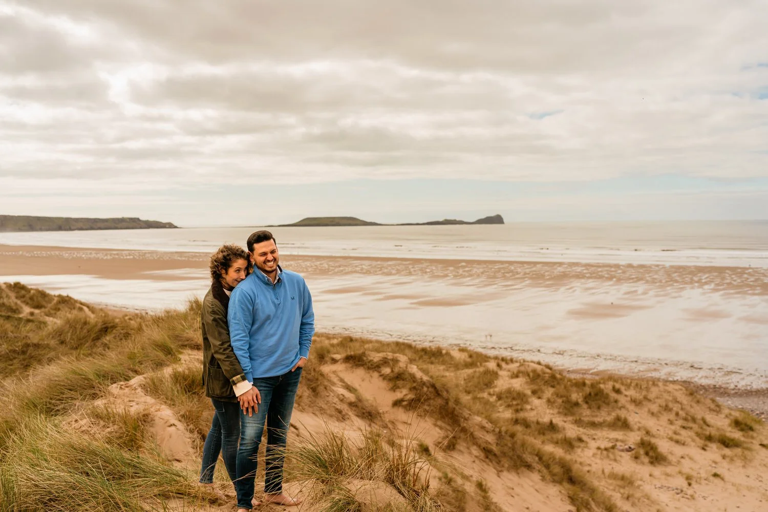 male and female engaged couple cuddling on top of sand dunes at Llangennith beach for their engagement pre wedding photographs.