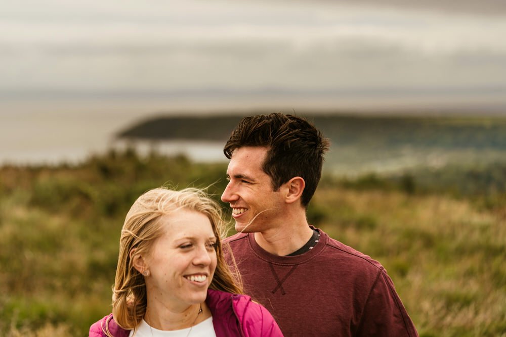 Male female couple posing during their wedding engagement session on Cefn Bryn with the view over Oxwich behind them.