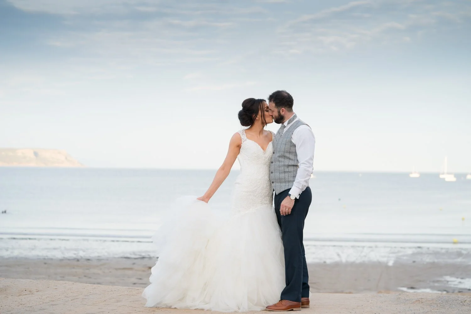Couple kissing on the beach in their wedding attire, just married at Oxwich bay hotel, the couple kissing with the sea behind them in South Wales. Taken during their wedding couples photo session.