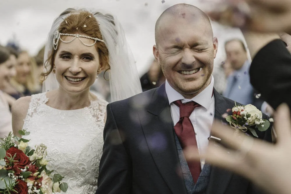 Happy wedding couple walking outside the Oxwich Bay Hotel in Swansea having confetti thrown over them