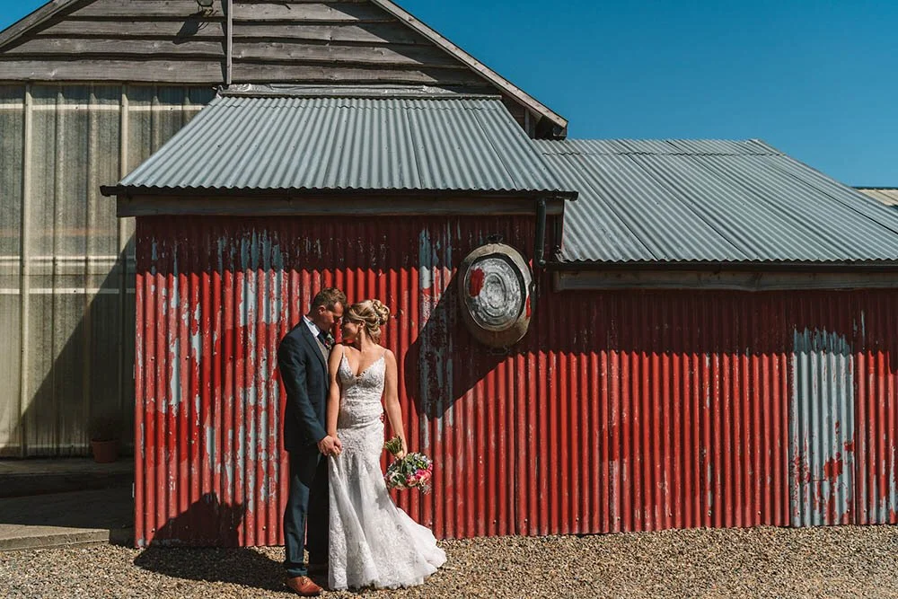 Woodhouse barn, a Newly wed couple outside the rustic industrial red barn at Rosemarket barn.