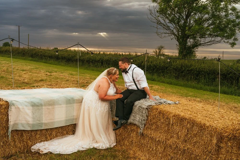 Wedding couple on hay bales at sunset. 