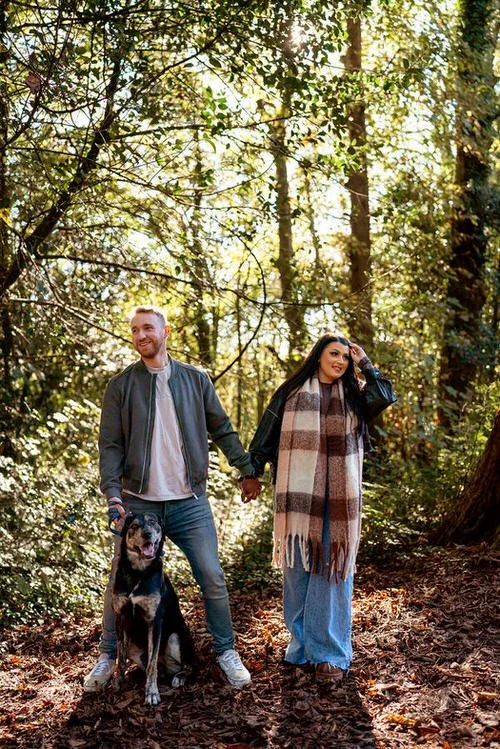 Engaged couple holding hands, stood in a sunlit forestry area with their dog, during their pre wedding photography shoot in Swansea.