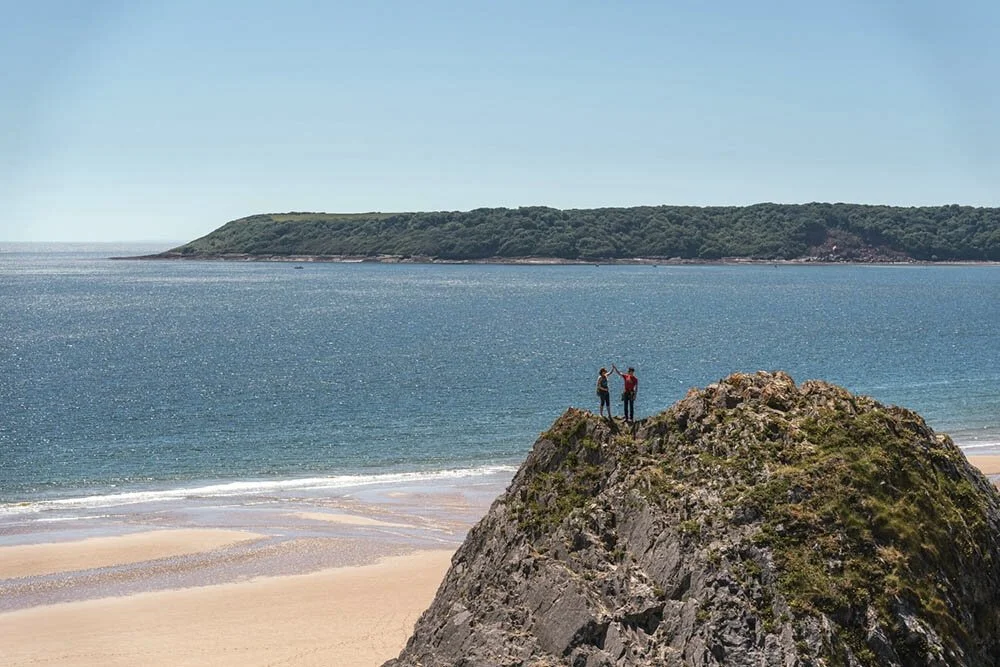 Two rock climbers high fiving each other at the summit of Three Cliffs in Gower.