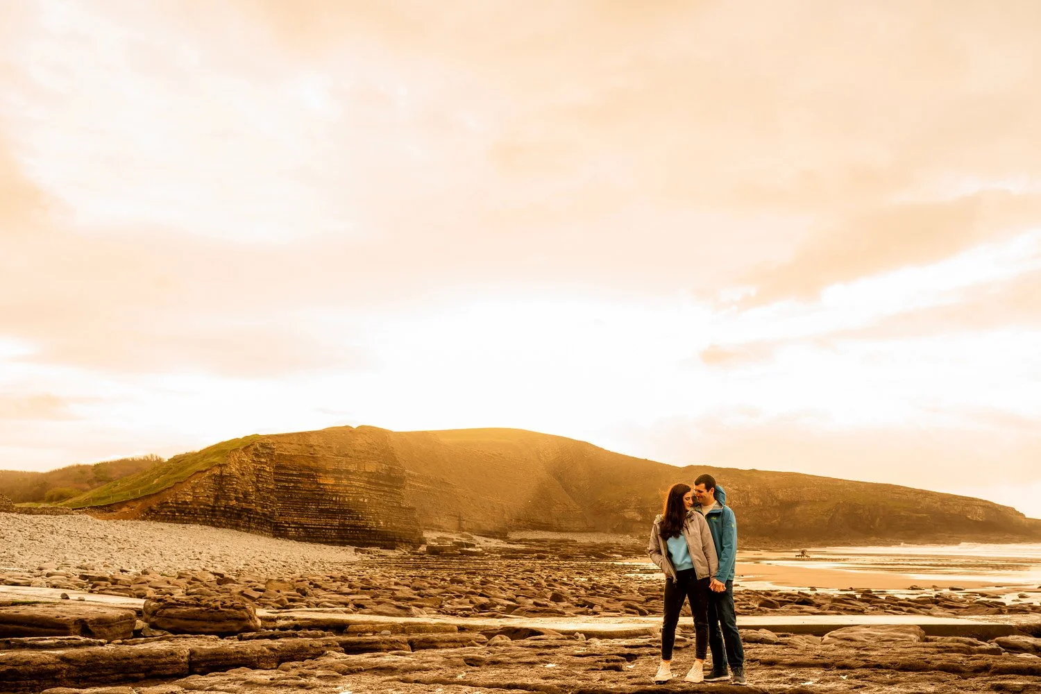 Engaged couple lit by sun flare on Dunraven bay.