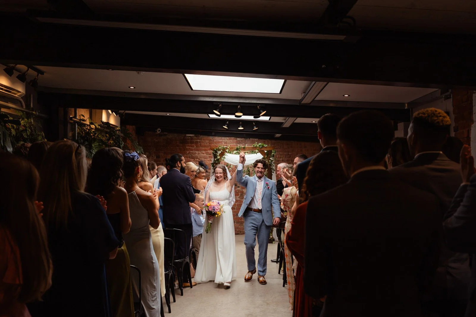 Excited wedding couple walking back down the aisle to cheers after getting married, inside the Shack Revolution Hereford