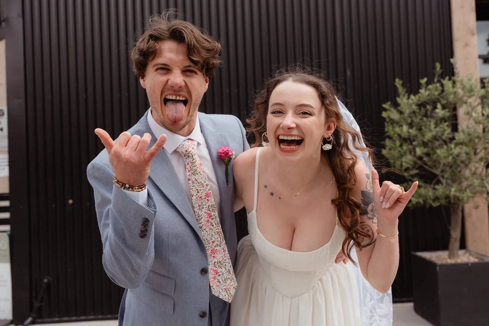 Wedding couple, male and female, outside the Shack Revolution wedding venue doing rock fingers, having fun for their couples portraits.
