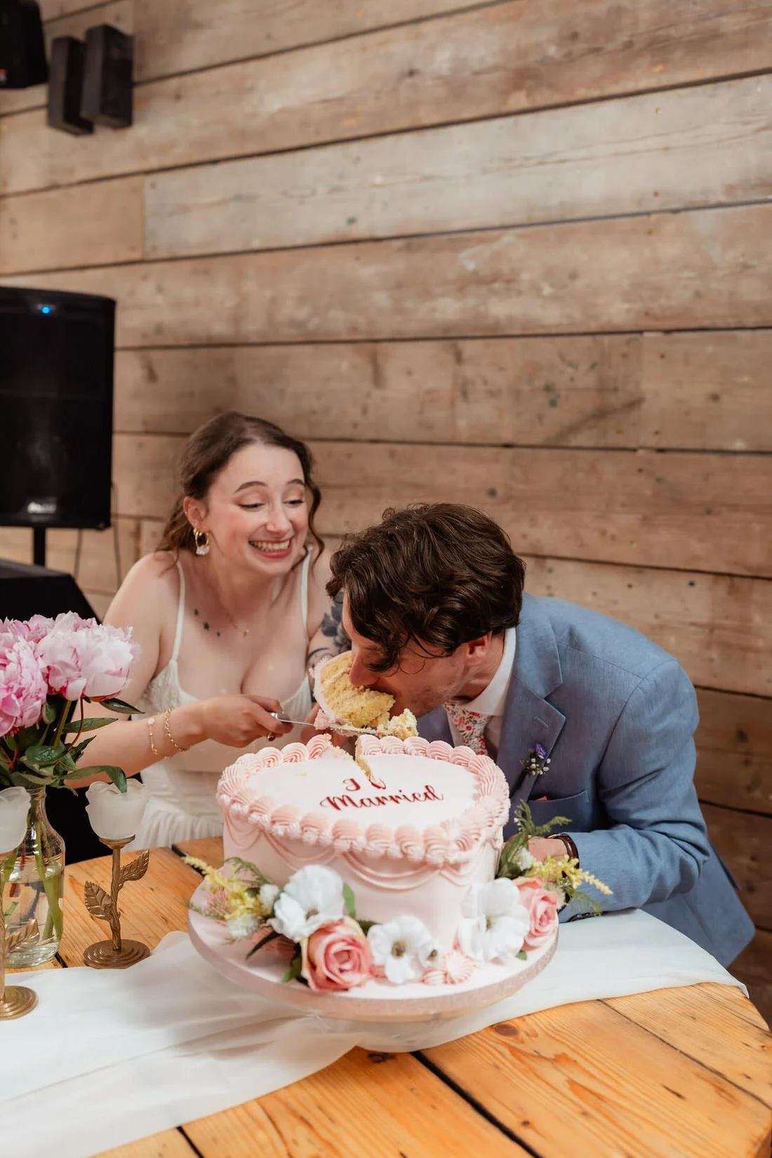 A bride laughs while feeding cake to the groom Inside Shack Revolution, Hereford, as he takes a big bite of their pink Just Married cake.