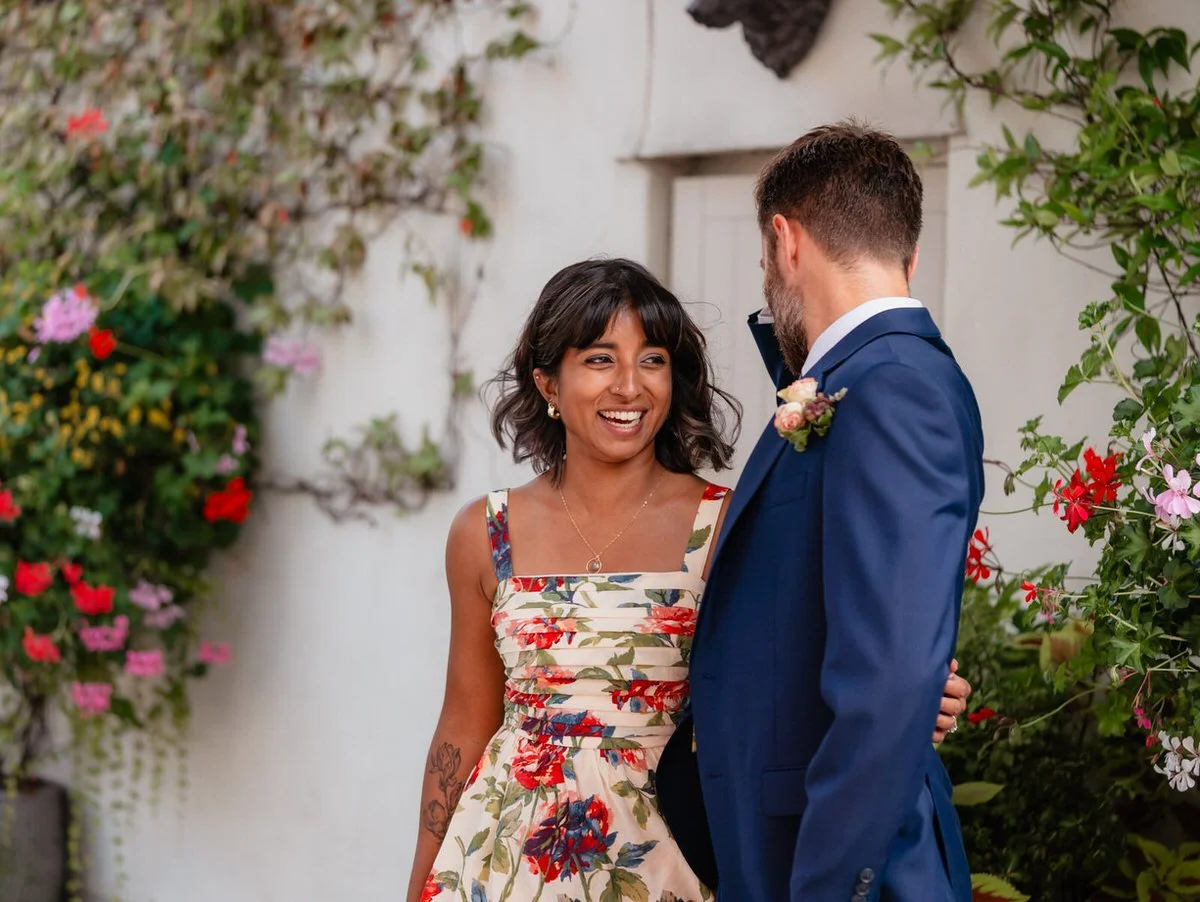 Colourful wedding guests enjoying themselves outside in the glass covered courtyard at the Bear Hotel in Cowbridge, a white wall with climbing flowers behind them