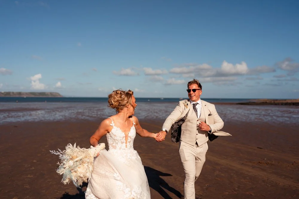 Happy wedding couple running along the beach at Oxwich for their fun wedding photos.