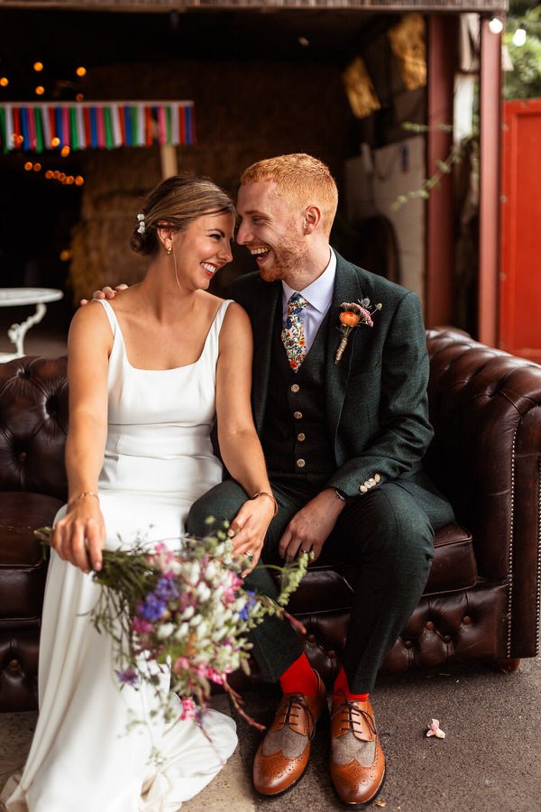 Happy smiling couple on their wedding day sat on a sofa laughter together at Sparkford Hall in Yeovil