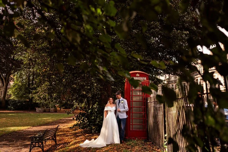 Newly married husband and wife in a Cardiff park next to a red phone box having their wedding photographs taken.