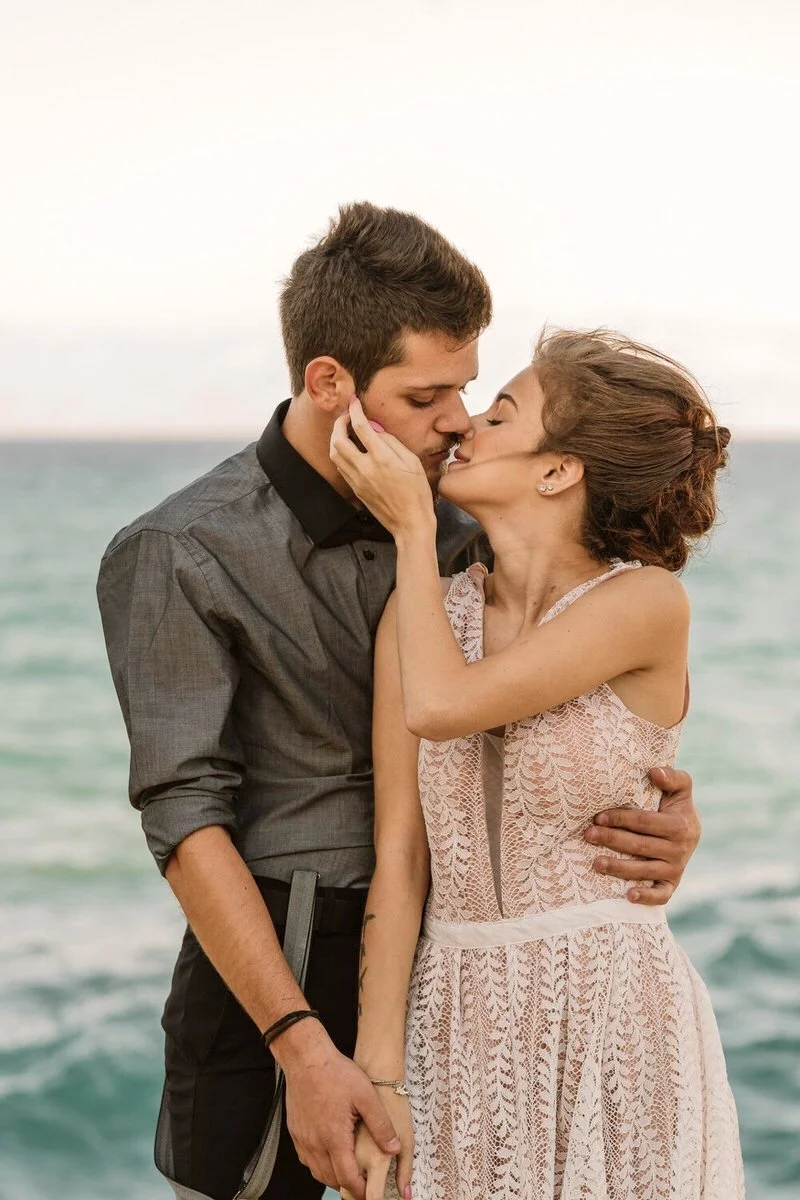 Bride and groom eloping to Corfu for their destination wedding, kissing on the edge of a cliff overlooking the ocean.