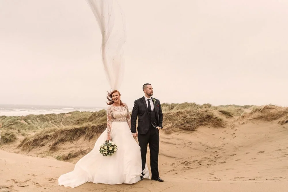 Wedding bride and groom couples photography in the windy location of Llangennith sand dunes, the brides cathedral veil blowing vertical in the wind.