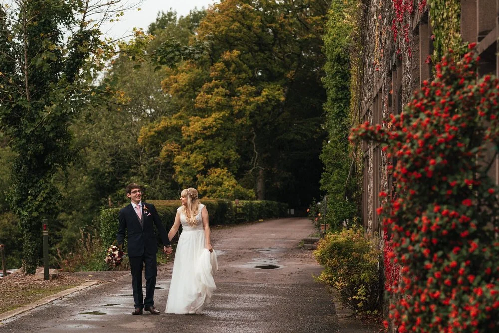 Happy wedding couple walking through the beautiful grounds at the Caer Llan wedding venue in Monmouth.