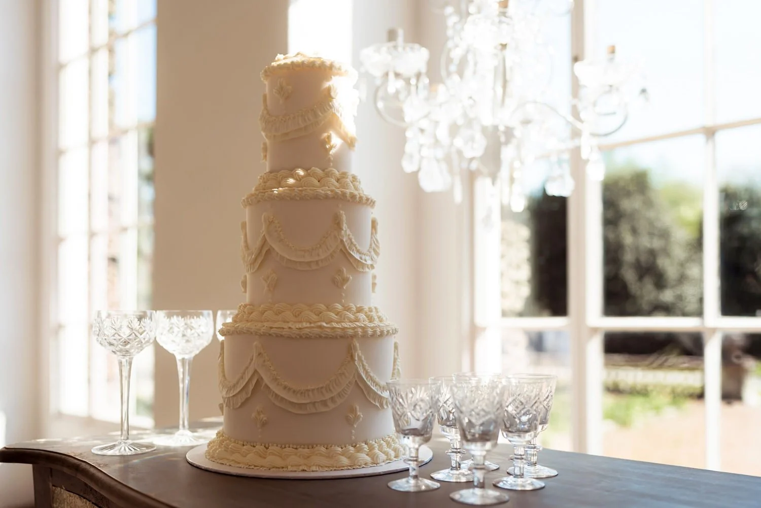 Crystal Moment  Elegant white wedding cake with piped detailing, surrounded by crystal glassware and chandelier in background