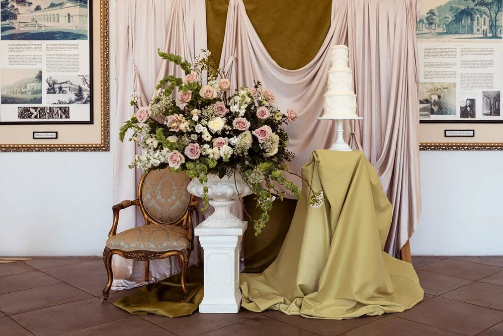 Bold Green Scape  Rich green draping and vintage-style decor with a tiered cake and dramatic floral styling