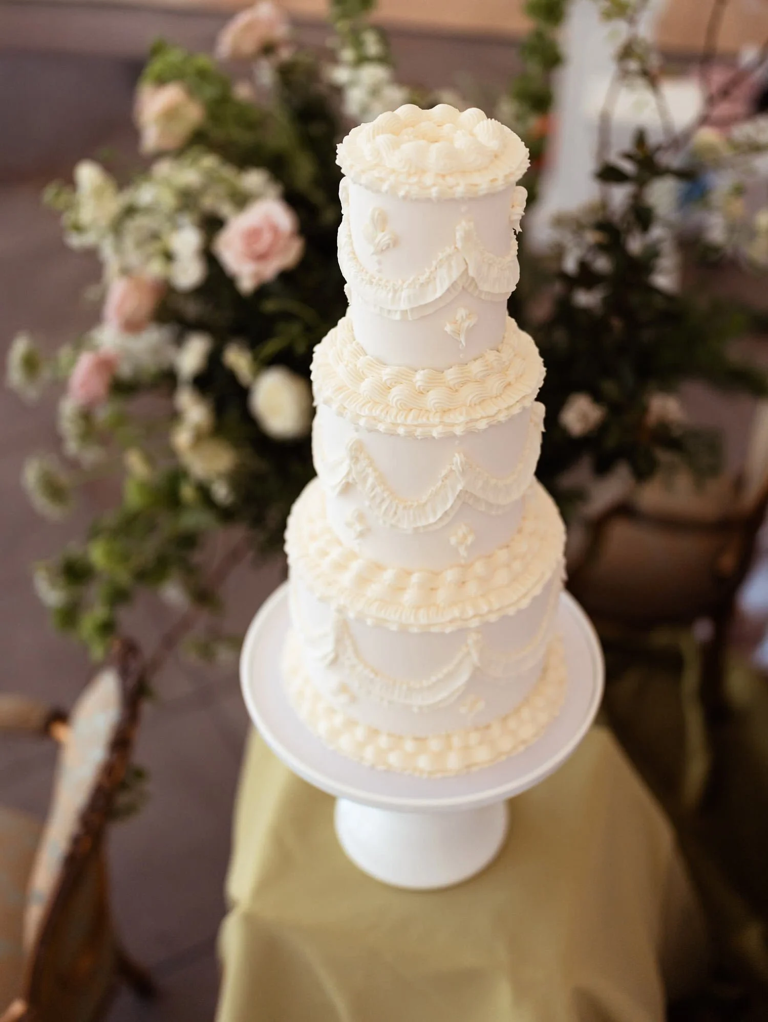 Piped highly detailed wedding cake with a floral display in the background.