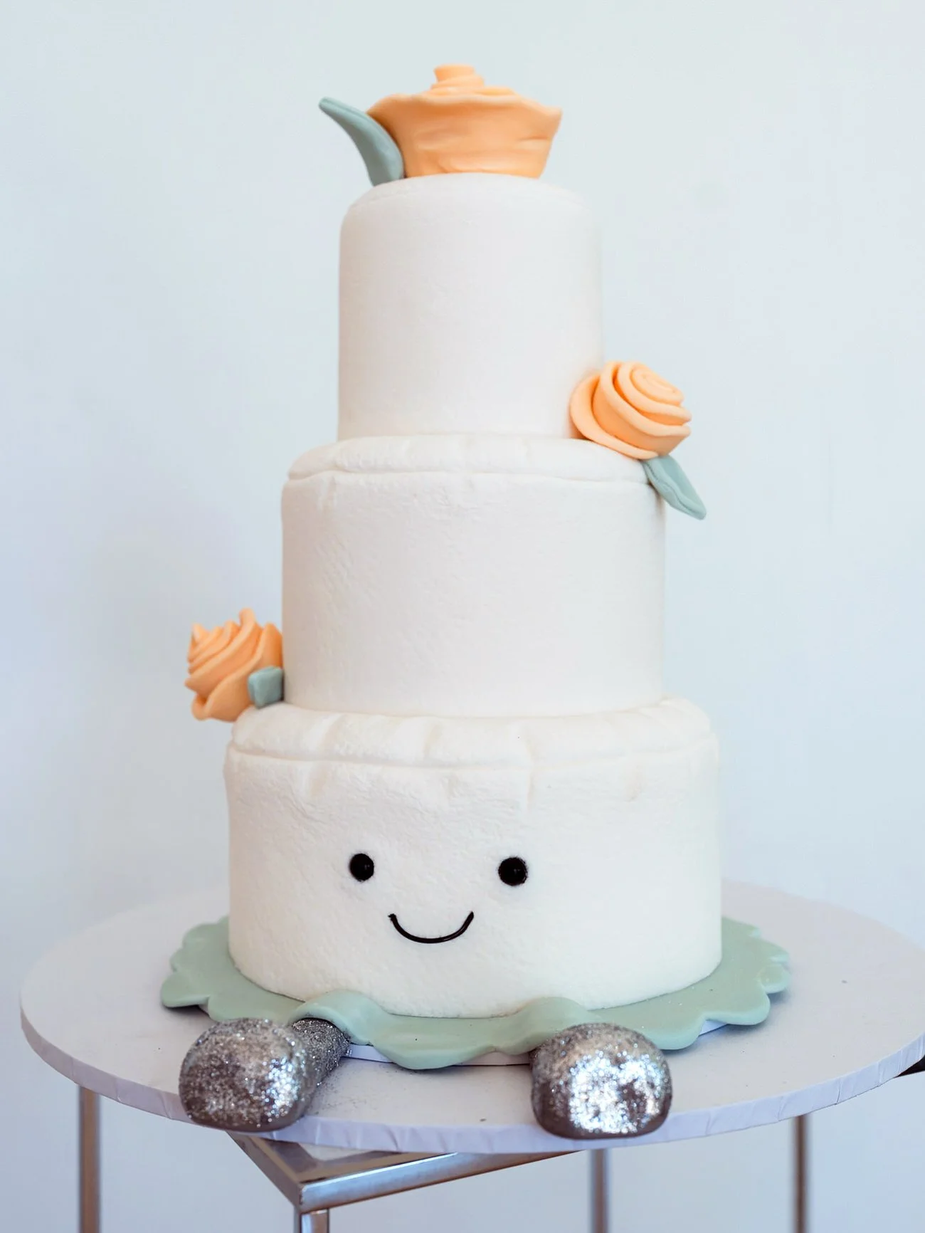 Cute three tiered wedding cake made to look like a marshmallow. An orange iced rose on each tier.
