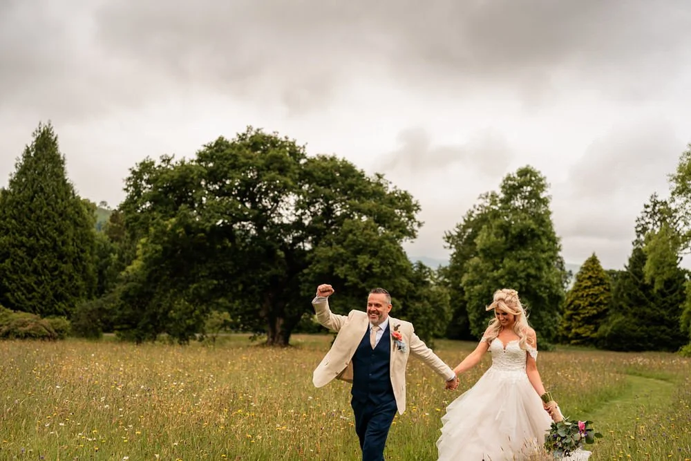 Excited bride and groom walking happily through a field of wildflowers in the grounds of Plas Dinam country house.