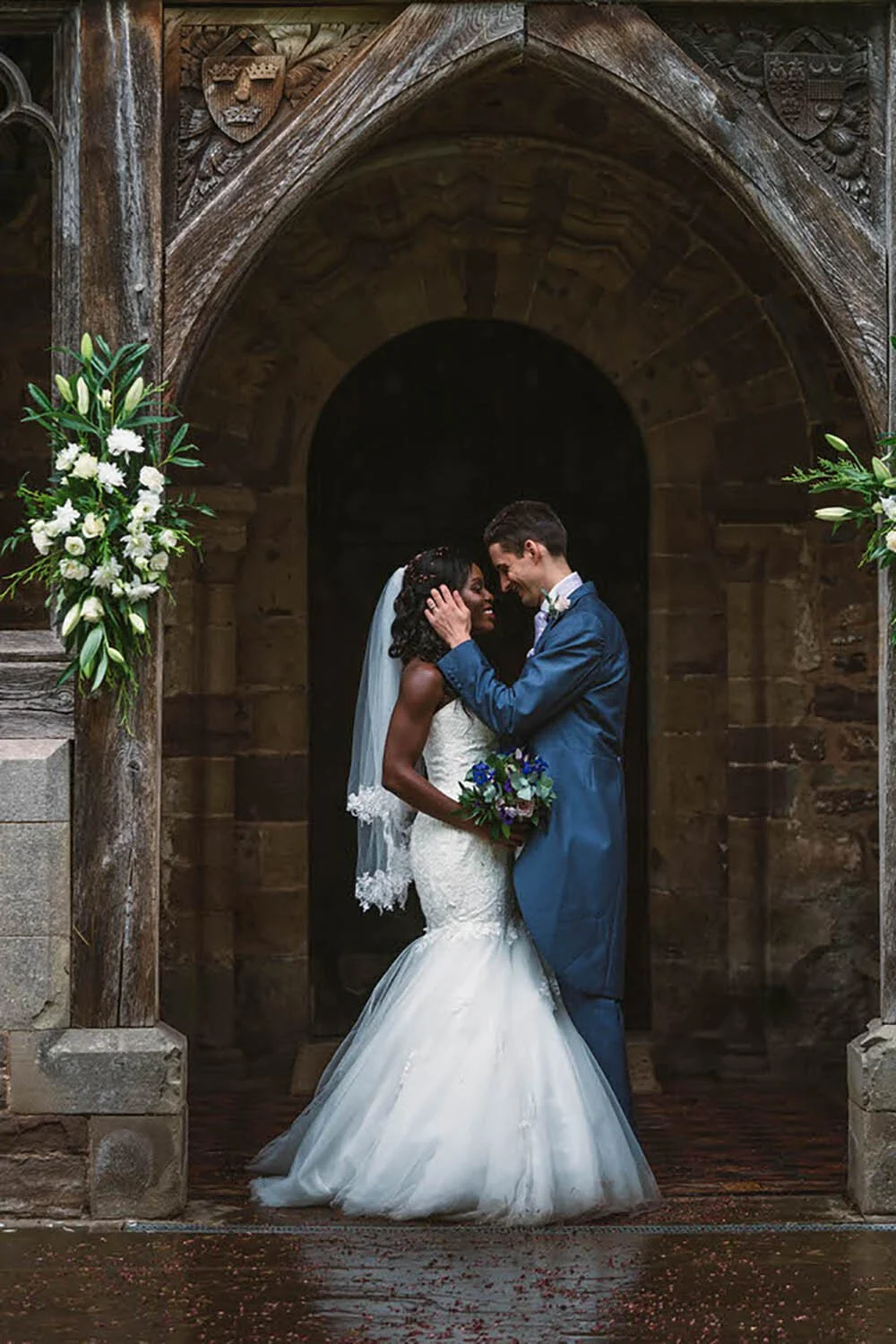 Married couple on their wedding day under the archway outside a church in Whitbourne. The groom stroking back the bride's hair in a happy romantic image.