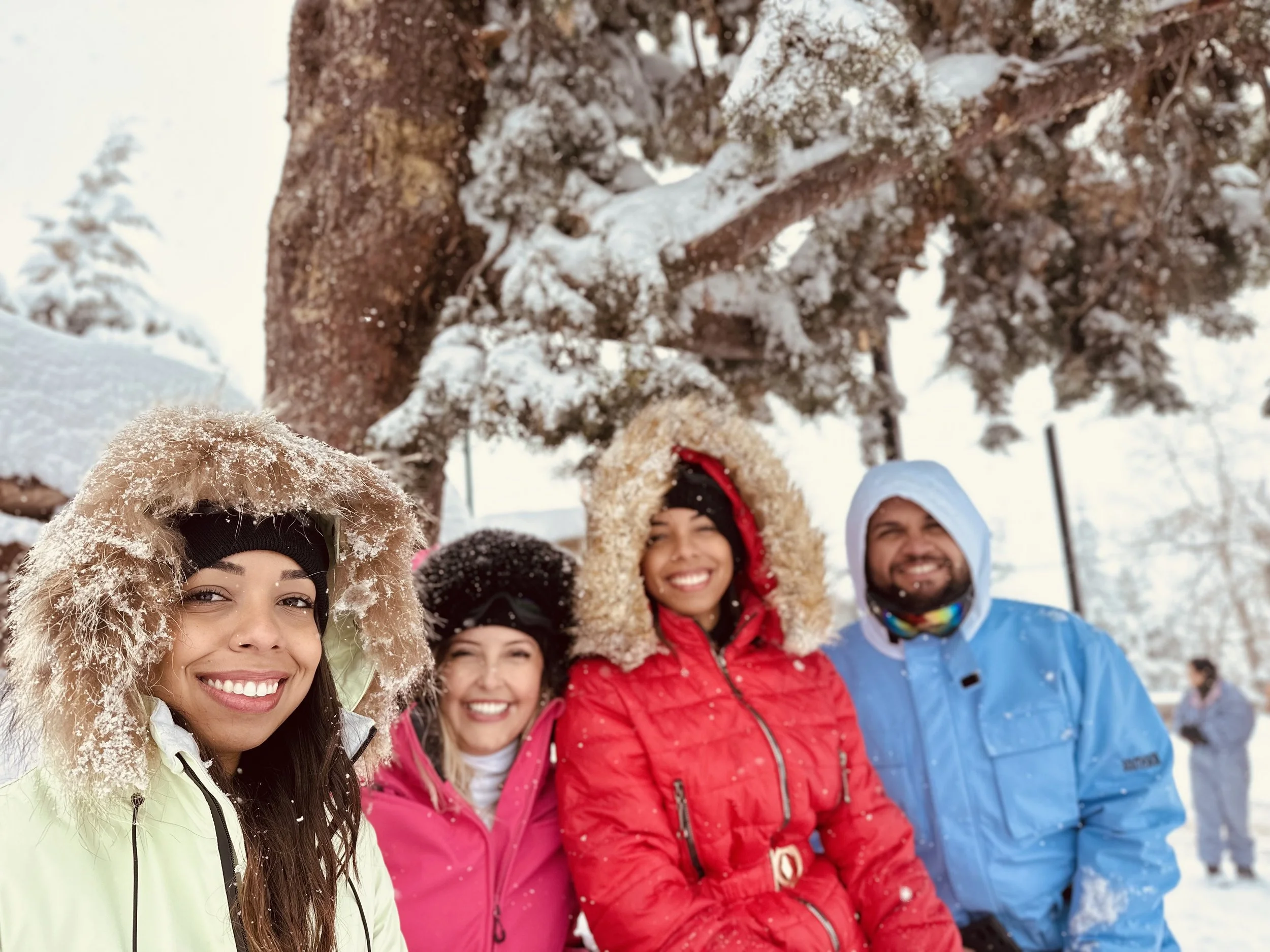 Pessoa de óculos de proteção e roupa de esqui relaxando em uma cadeira de teleférico na neve, com pista de esqui, redes de proteção e uma cabana vermelha ao fundo, em ambiente de estação de esqui.