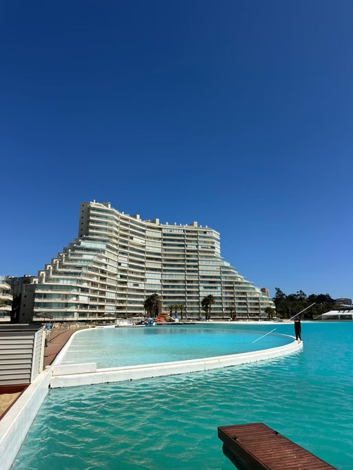 Piscina com vista para um prédio de arquitetura moderna e curvas, sob céu azul.