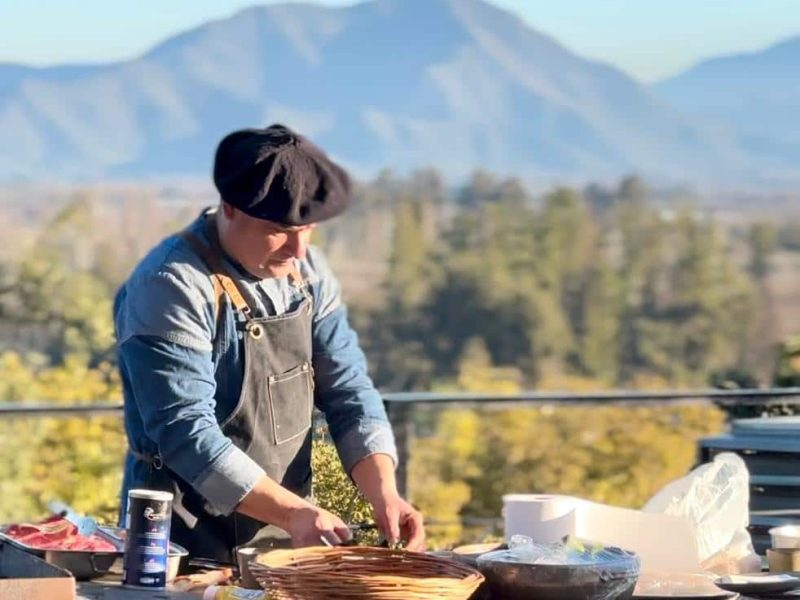Pessoa preparando comida ao ar livre com uma montanha ao fundo.