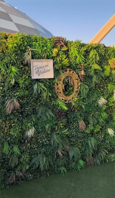 Parede decorativa de plantas verdes com espelho dourado e placa que diz "Toque para Voar".
