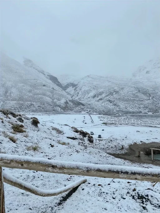 Paisagem de montanha coberta de neve com estradas e veículos, céu nublado.