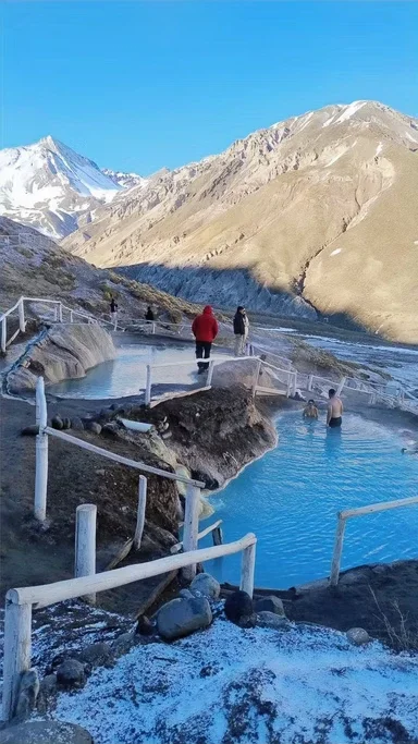 Piscinas termais ao ar livre em uma área montanhosa, com pessoas relaxando e desfrutando do ambiente, com montanhas ao fundo.