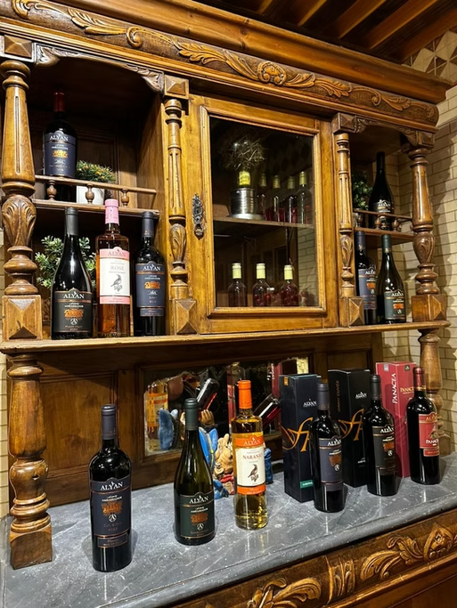 Vitrine de madeira com várias garrafas de vinho e uma garrafa de whisky, além de caixas de presente de vinho, em uma superfície de pedra.