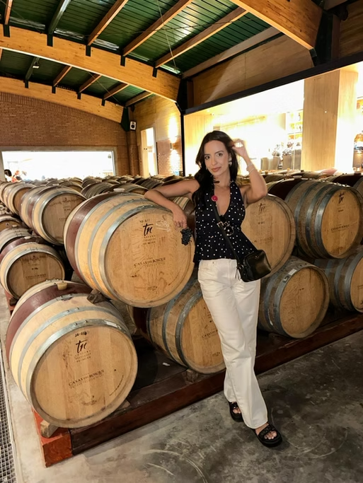 Mulher posando ao lado de barris de carvalho em uma adega de vinho.