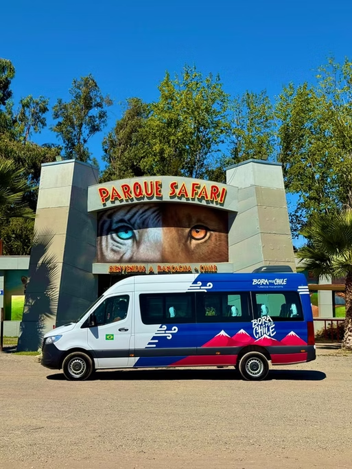 Entrada do Parque Safari com um voucher de um ônibus de turismo ao fundo, sob céu azul.