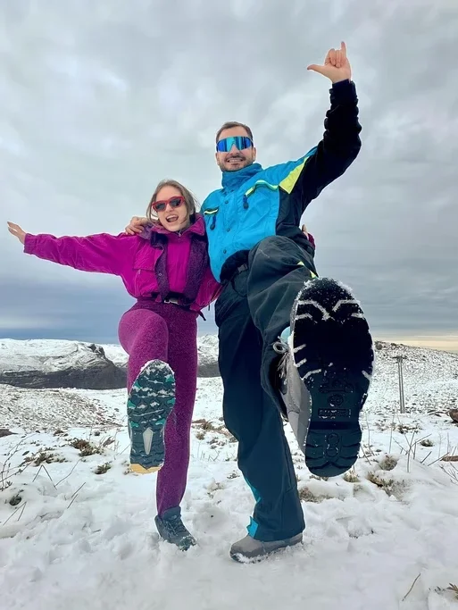 Homens e mulheres sorrindo e pulando na neve com roupas de inverno.