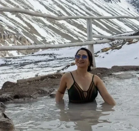 Mulher sorrindo em uma piscina com fundo de montanhas nevadas
