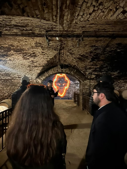Pessoas em uma caverna com uma fogueira decorativa em forma de rosto ao fundo.