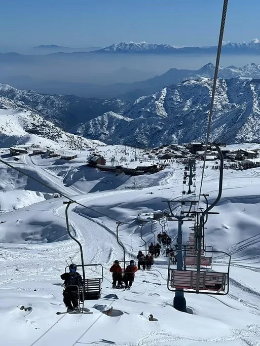 Paisagem de estação de esqui com cadeiras de teleférico subindo montanhas cobertas de neve, fundos de montanhas e céu claro.