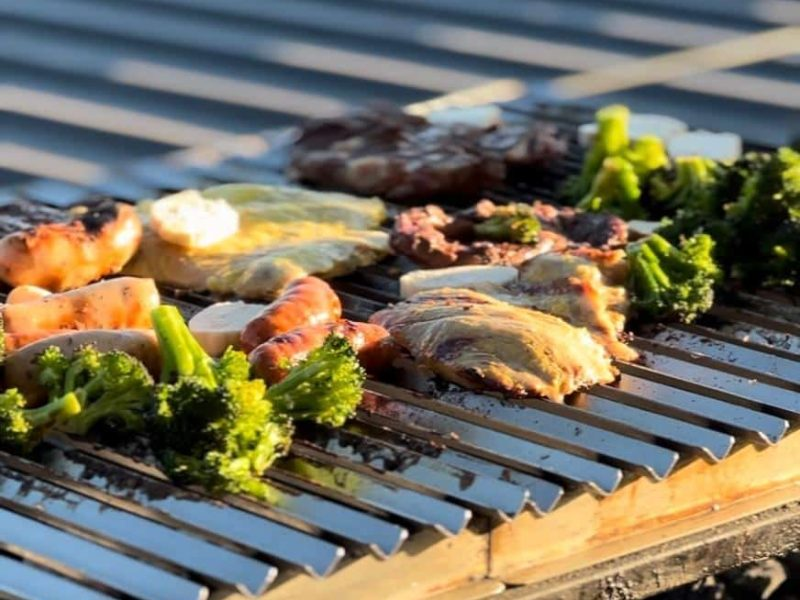 Carnes e legumes grelhados em uma churrasqueira de metal.