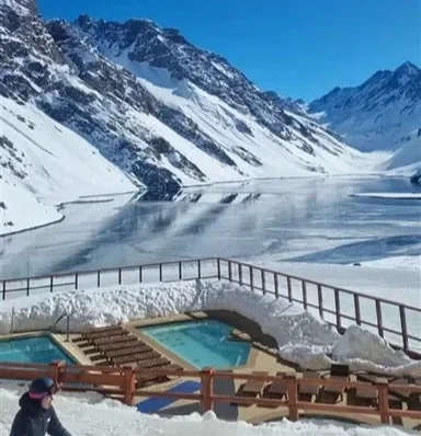 Piscinas ao ar livre em uma paisagem de montanhas nevadas e um lago congelado com uma cerca de proteção.