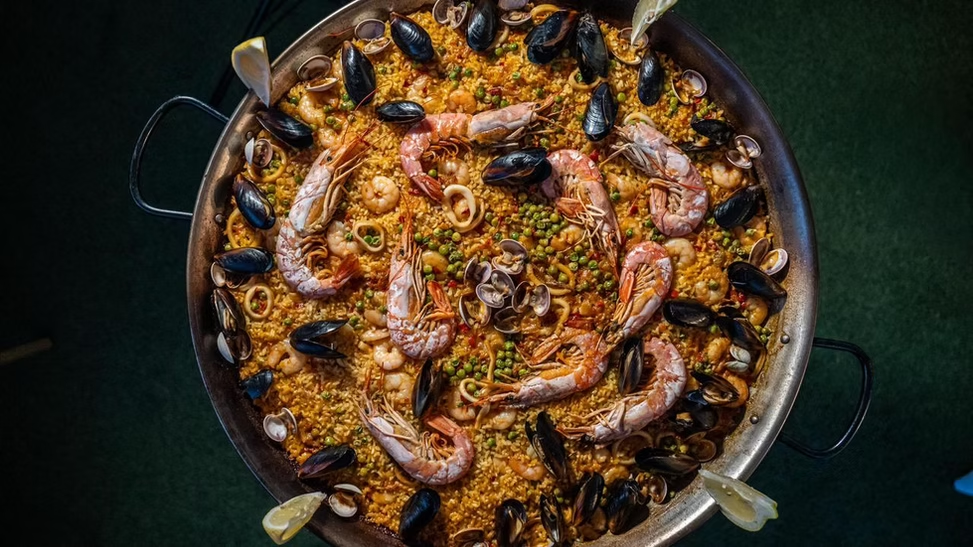 Paella de frutos do mar com camarões, mexilhões, arroz e legumes, em uma panela grande.