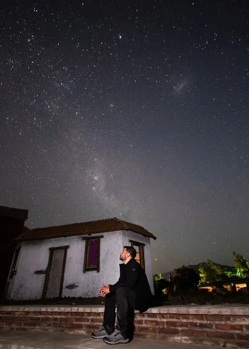 Homem sentado na varanda de uma casa observando o céu estrelado à noite.