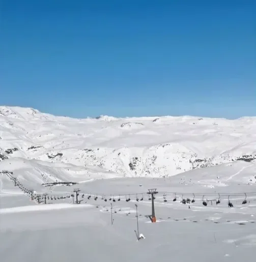 Estação de esqui com cadeiras de teleférico suspendidas sobre a neve, em uma paisagem montanhosa coberta de neve sob um céu azul