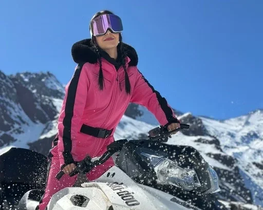 Mulher com roupa de esqui rosa e óculos de proteção em uma moto de neve nas montanhas com neve.