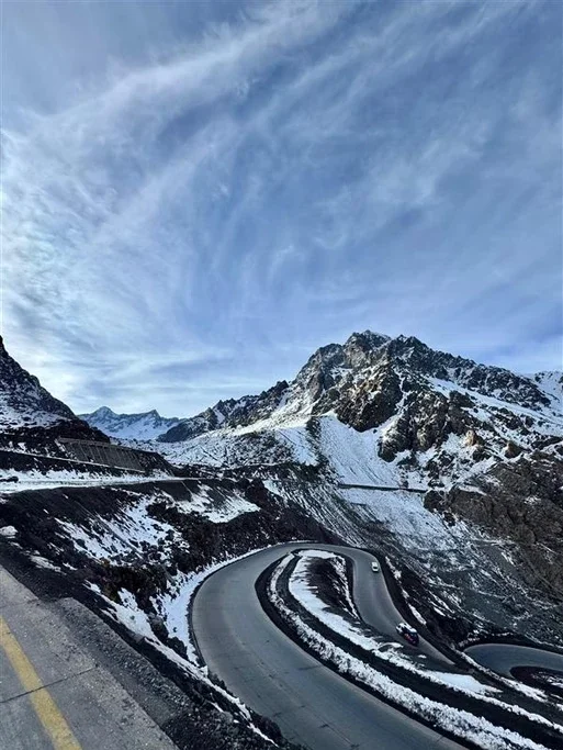 Estrada sinuosa nas montanhas com neve e céu com nuvens.