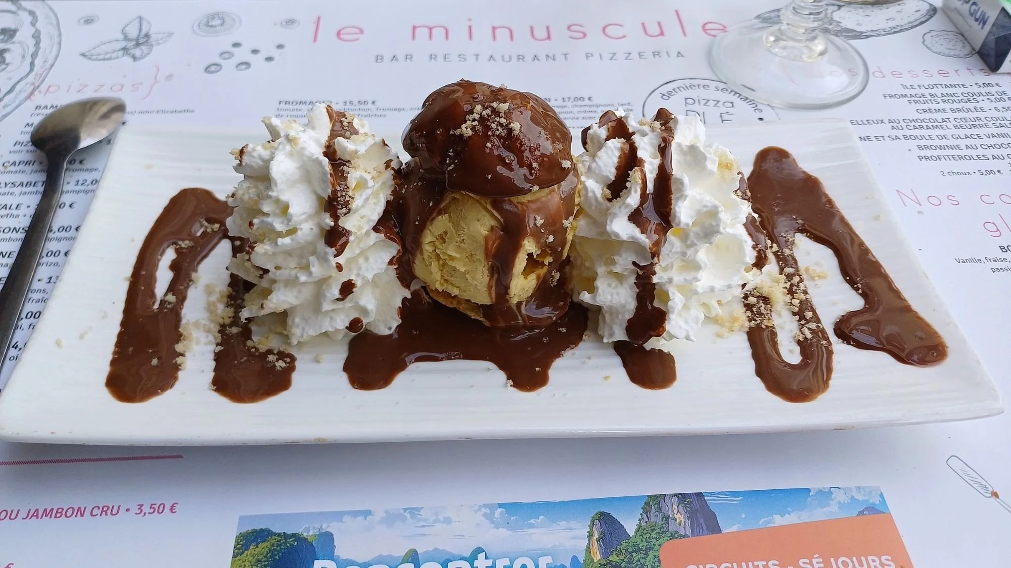Chocolate-drizzled profiterole dessert served on a plate at Le Minuscule restaurant in Châteaulin, France.
