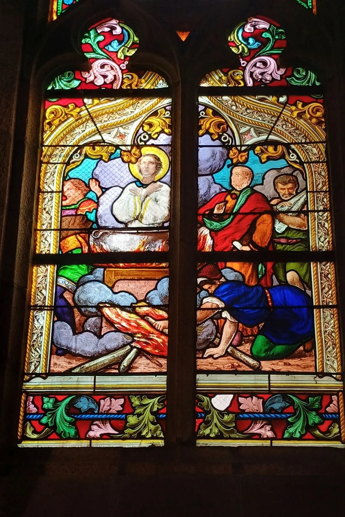 Stained glass window inside Église Saint-Idunet in Châteaulin depicting a haloed saint praying calmly over a burning cauldron.