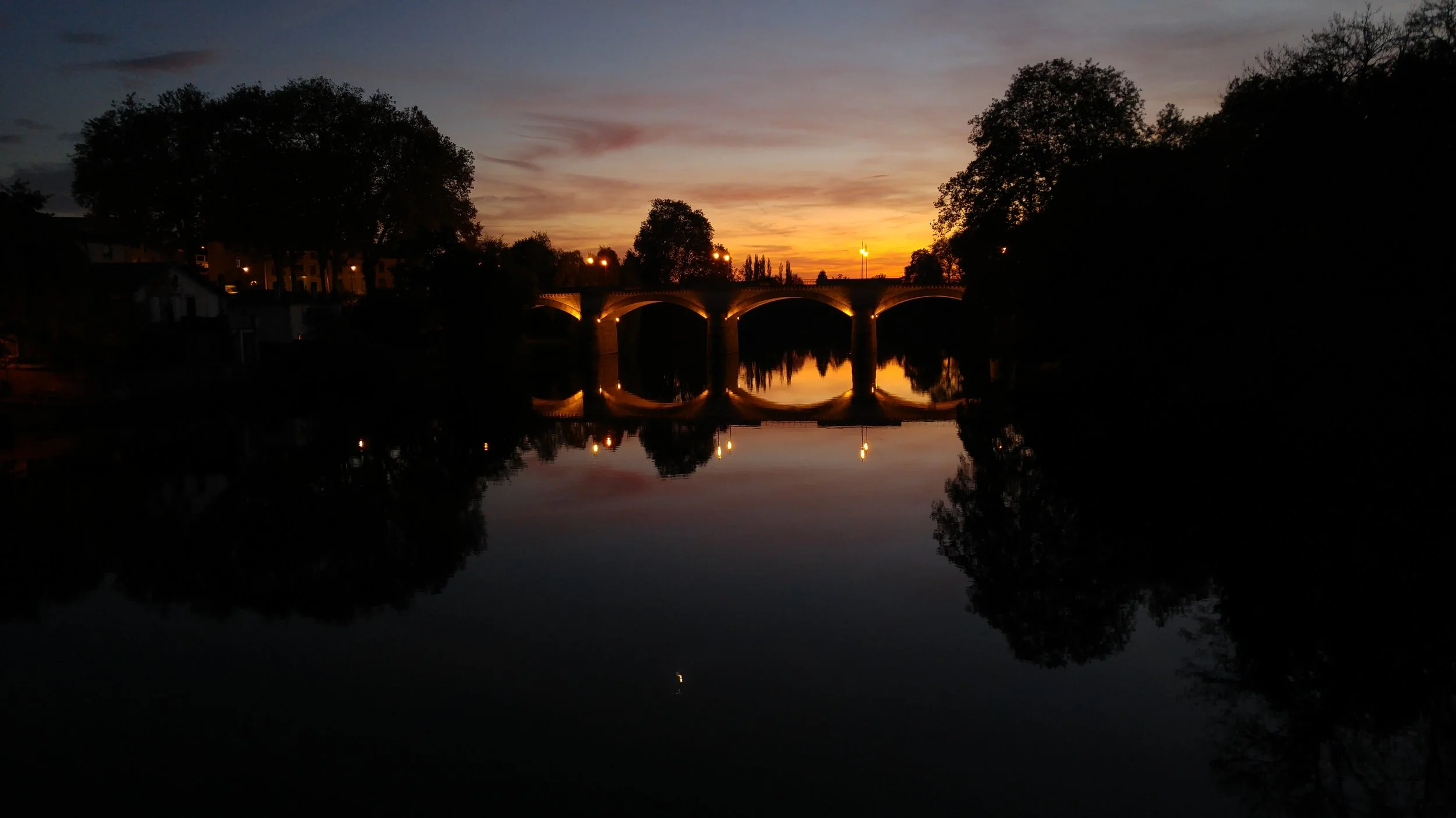 The sun sets over the Vienne River in Confolens, France, with the D948 bridge visible in the background as night falls over this quiet western French town.