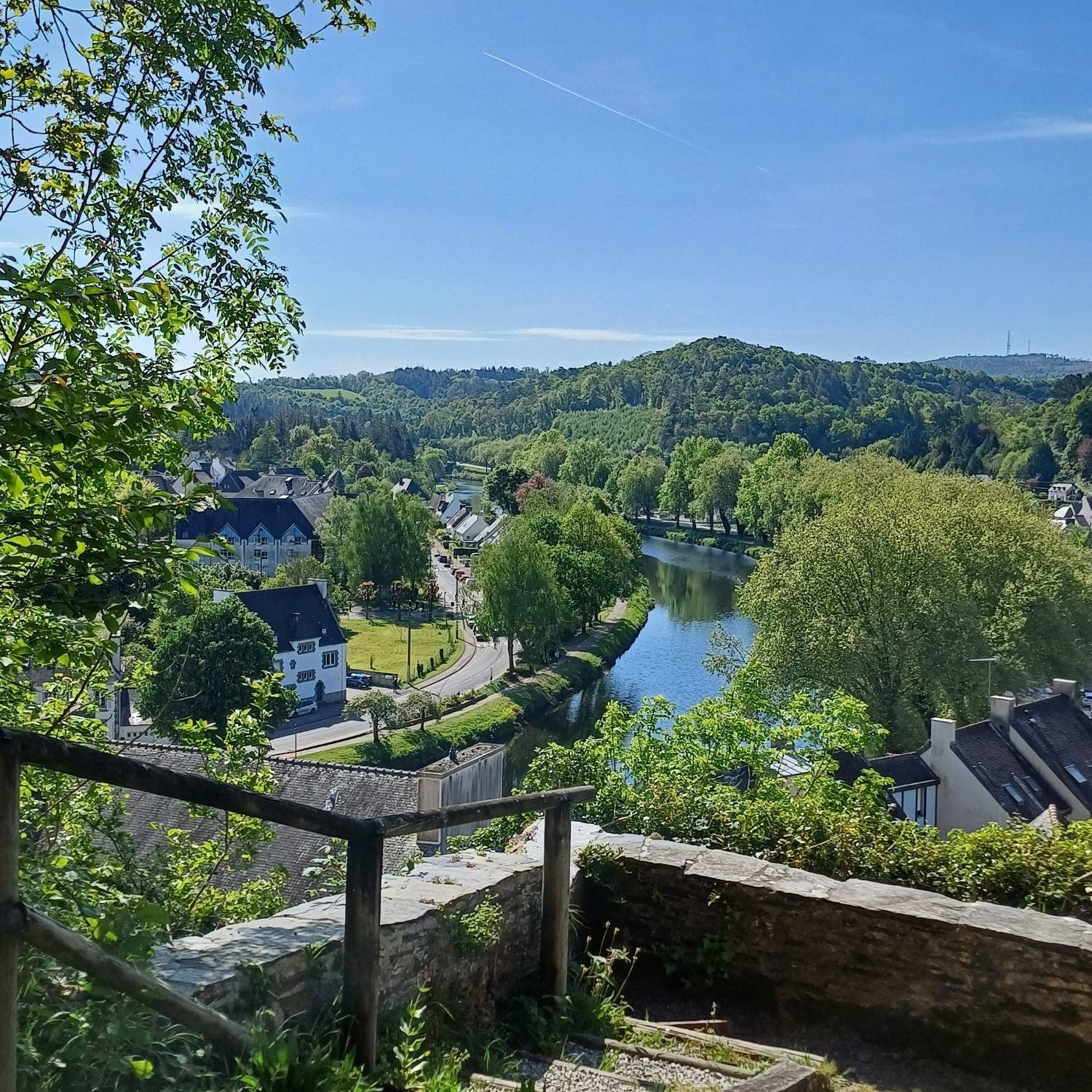 Hilltop view of Châteaulin, France and the Aulne River from the Chapelle Notre-Dame showcasing a blue sky and lots of green trees.